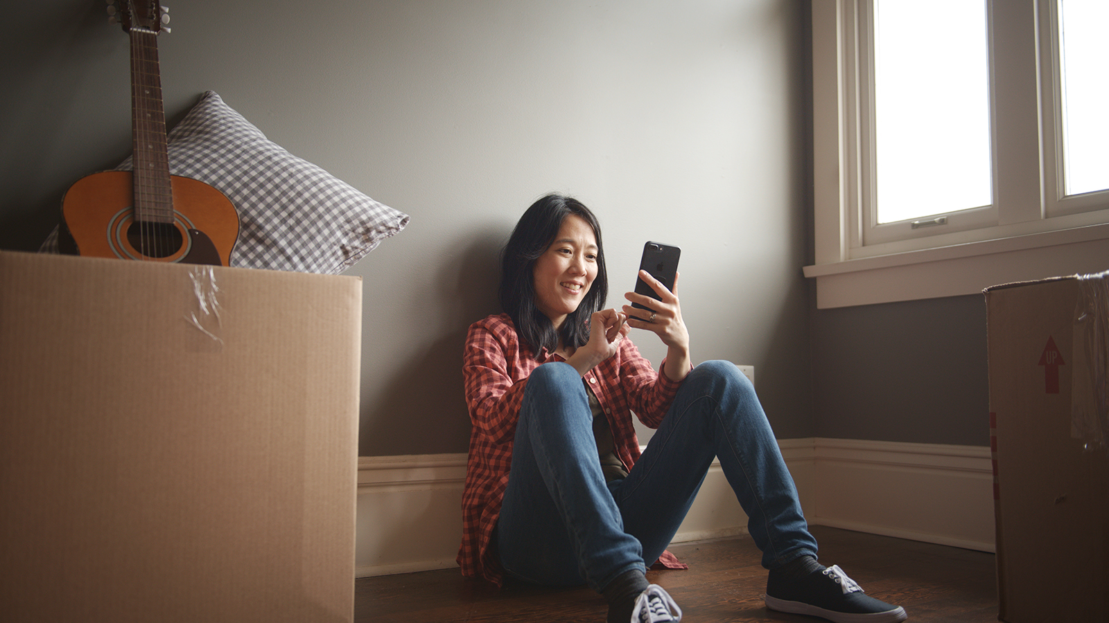 a woman sitting on a floor looking at her phone surrounding by boxes