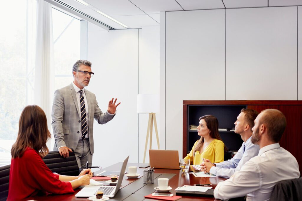 Confident mature businessman discussing with colleagues at conference table in office meeting