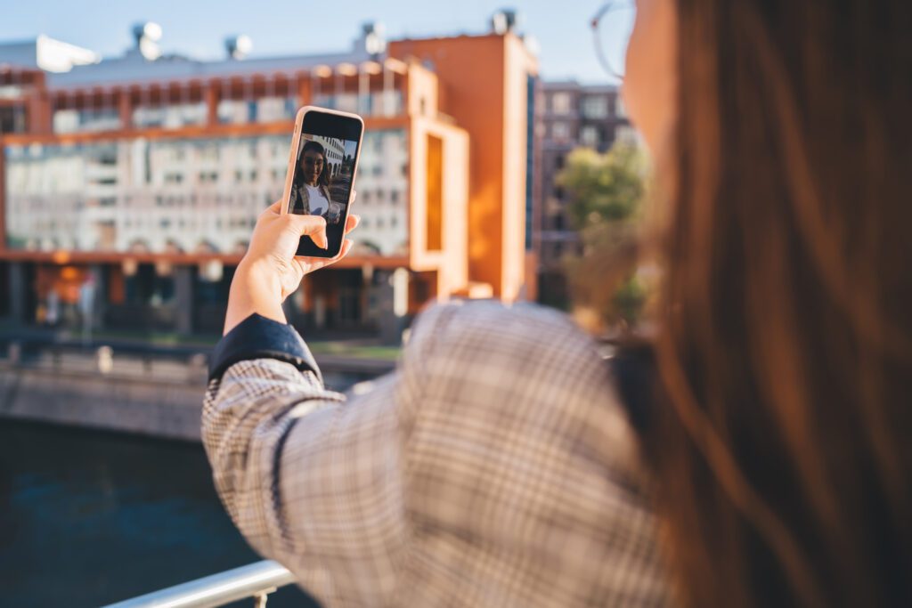 Xfinity Mobile customer in Indiana utilizing new Premium Unlimited plans 4K streaming and hotspot data on WiFi. IMAGE: Back view of female traveler using smartphone camera for taking online video for vlog in social networks, smiling woman making facetime call using 4G connection in roaming during journey in city.