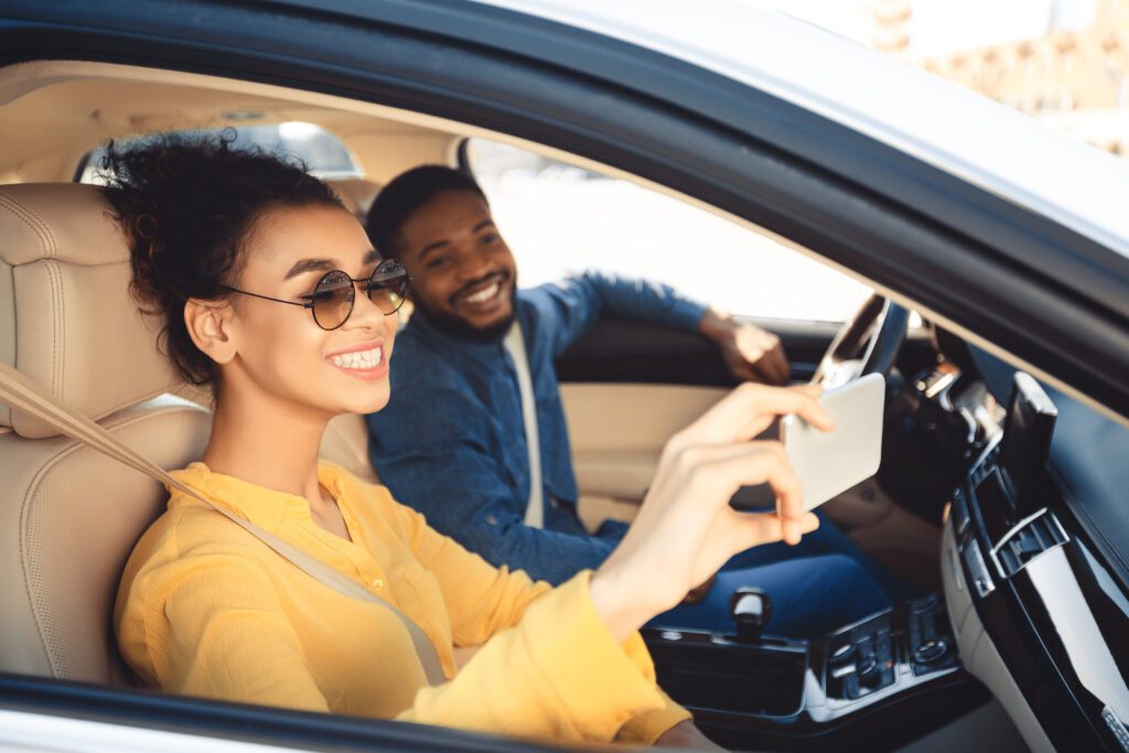 Couple in car using mobile device to find Black Friday and Cyber Monday holiday savings while on the road.