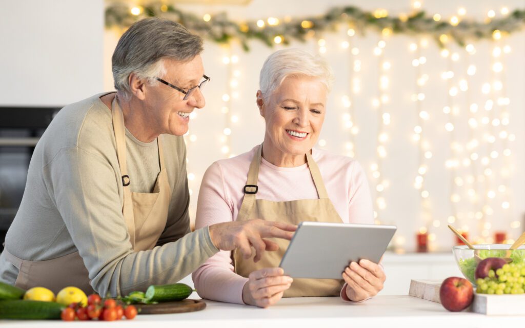 Older adults in festive kitchen using tablet to explore holiday deals and Cyber Monday savings together.